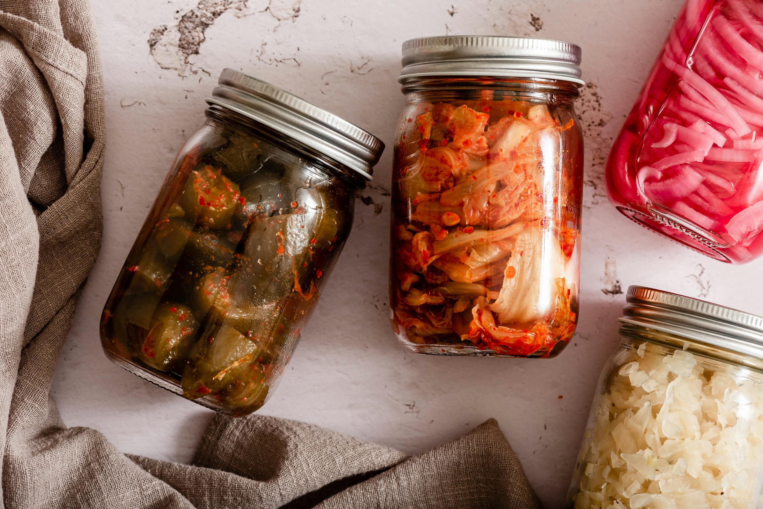 Jars of kimchi, kefir, sauerkraut and kombucha arranged on a kitchen shelf