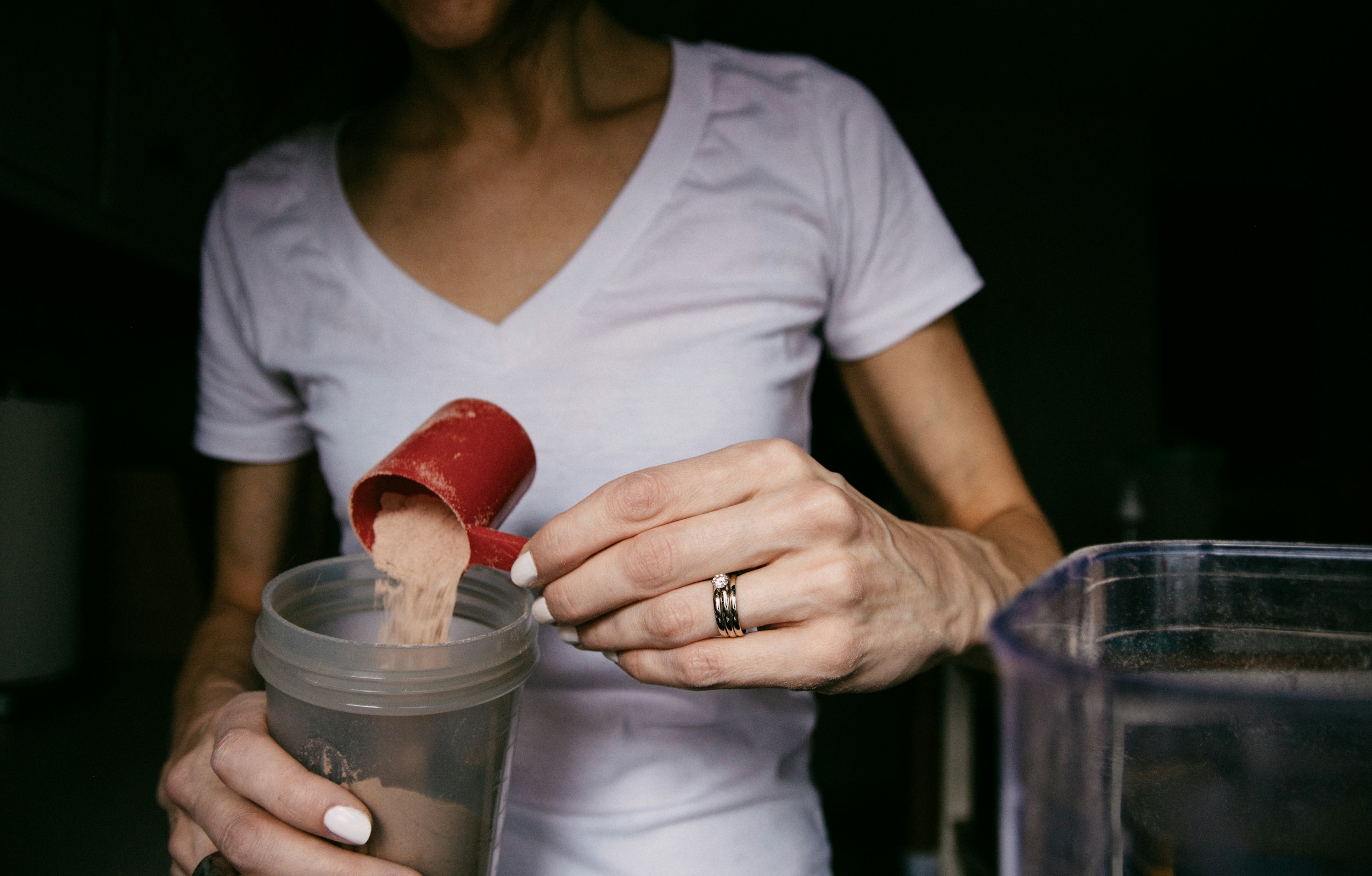 White powder supplement in a wooden spoon next to a glass of water on a clean kitchen surface